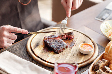 the man in the restaurant with a knife cuts steak of marble beef, grilled. Serving on a wooden Board.