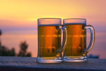 2 mugs of beer on the sunset background