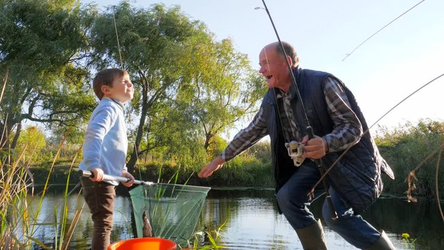 family fishing on lough, old man with kid have good time on fresh air in spring among green trees and reeds