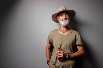 Cheers! Vacation concept. Studio portrait of handsome senior man with gray beard and hat holding...