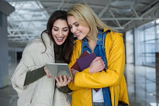 Attractive women laughing while looking at tablet. One is pointing at device and other holding books