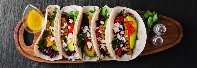 Mexican tacos with avocado, grilled corn, red cabbage slaw and chili salsa on wooden board black...