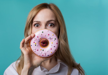 Tasty calories. Portrait of beautiful lady holding pink donut before her mouth and looking at...