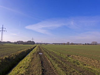 Fototapeta na wymiar Reifenspuren auf einem matschigen Feldweg, blauer Himmel. Ein sonniger kalter Tag