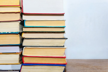 Stack of different books on a table against a white wall background