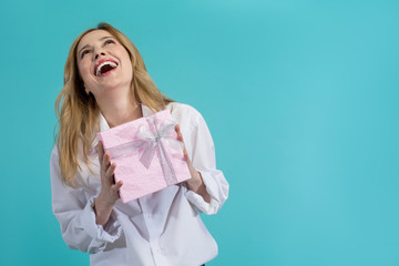 Portrait of happy blonde girl holding present and laughing. Copy space in right side. Isolated on blue background