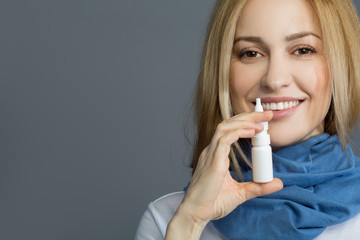 Portrait of smiling girl in blue scarf holding nasal spray. Isolated on background. Copy space in...