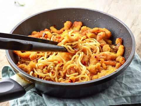 Asian noodles with fried meat on cooking pan
