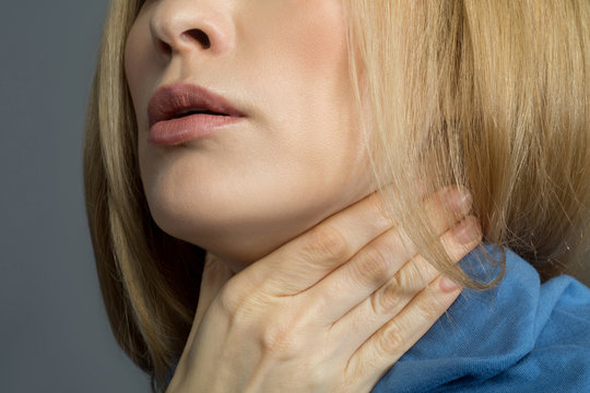 Sore throat. Close up of female chin, lady is holding her hand on neck covered with scarf. Isolated on background