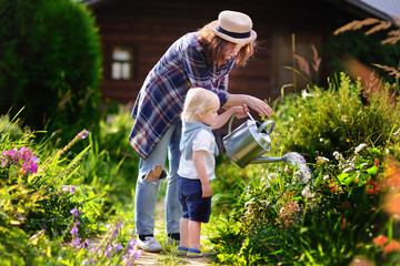 Toddler boy and his young mother watering plants in the garden