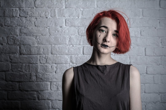 Portrait. Teenage girl with bright red hair at the white wall. On the face of the girl makeup.
