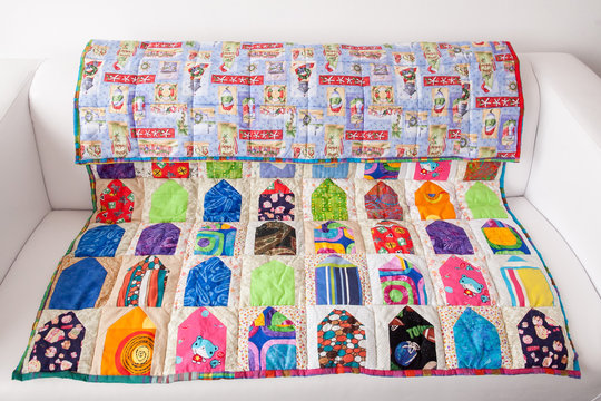 interior, quilting, handcraft concept. on the small couch of light creamy colour there is extremely bright blanket with two absolutelu different sides, it is sewed of various pieces of fabrics