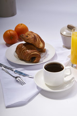 Fresh croissants, orange juice, coffee and oranges. Continental breakfast on white table