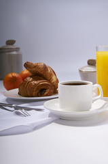 Fresh croissants, orange juice, coffee and oranges. Continental breakfast on white table