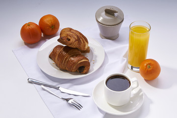 Fresh croissants, orange juice, coffee and oranges. Continental breakfast on white table