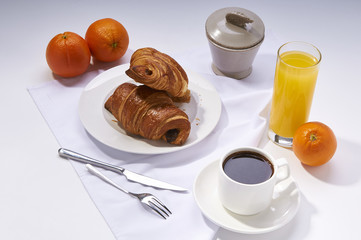 Fresh croissants, orange juice, coffee and oranges. Continental breakfast on white table