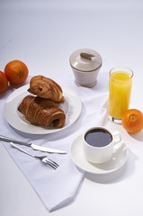 Fresh croissants, orange juice, coffee and oranges. Continental breakfast on white table