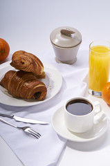 Fresh croissants, orange juice, coffee and oranges. Continental breakfast on white table