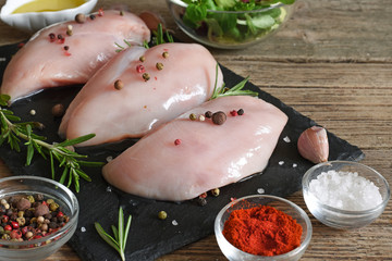 Raw chicken breasts fillet witn rosemary and spices on black slate cutting board