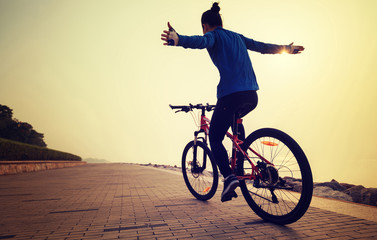 Obraz premium cyclist riding bike with arms outstretched in the coasts sunrise sunshine wellness concept