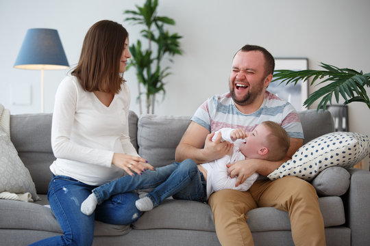 Photo of happy pregnant wife, husband and son on gray sofa