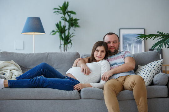 Photo of happy pregnant woman and man on gray sofa