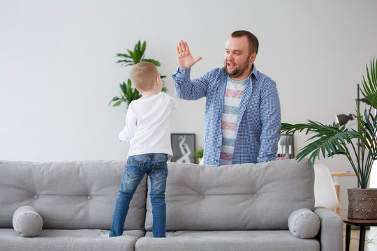 Family image of young son standing on sofa making handshake with dad
