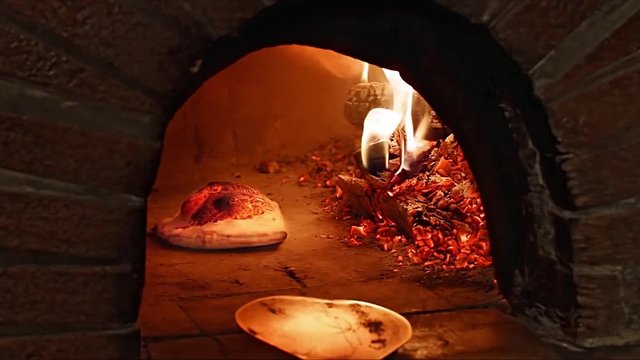 pizza baker loading crispy pizza calzone into wood fired stone oven with pizza peel