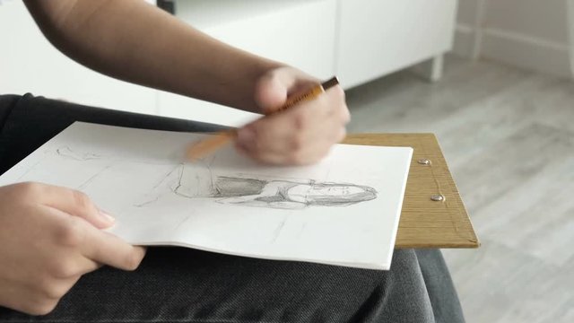 Young woman working on a project, drawing and thinking. Workspace designer. White sheet of paper, pencils. Female fashion artist drawing sketches. Close-up
