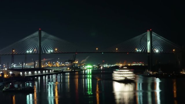 A night time lapse view of river traffic passing under the Talmadge Memorial Bridge over the Savannah River in Georgia.  	
