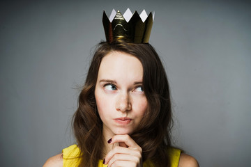 A young pensive girl with a golden crown on her head thinks about Mother's Day