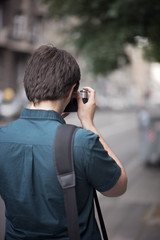 Young attractive man, a photographer, taking photographs in an urban area with an analog SLR camera