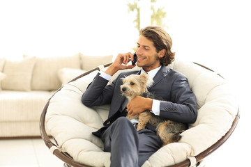 businessman holds his pet and talks on the smartphone while sitting in a comfortable chair