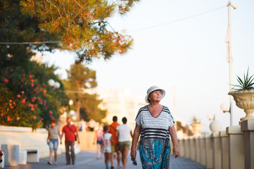 Elegant mature woman walking on promenade during summer sunset in park