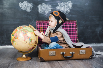 boy pilot sitting in a suitcase with a globe
