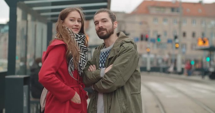 Smiling couple looking away while waiting at tram stop in a city.