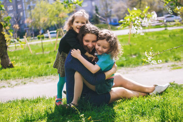 Fototapeta premium Little girl hugs mother sitting on the grass. Child, playing, threw his mother on grass.