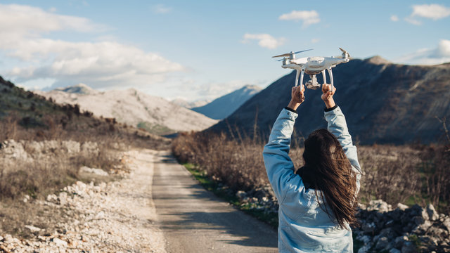 Young woman videographer catching flying aircraft with camera.Controlling landing of drone.Female filmmaker in nature using quad copter aircraft to capture landscape.Assisting drone landing.