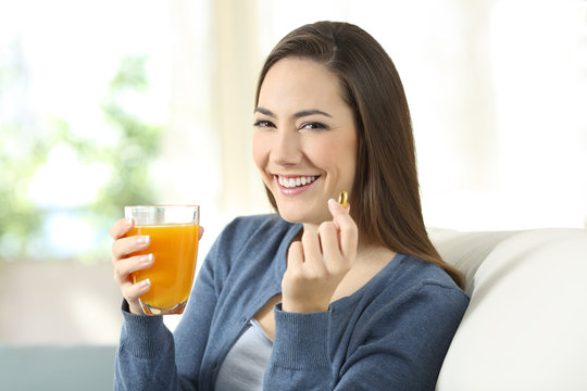 Girl holding an orange juice and a pill looking at you