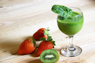 Fresh, healthy, homemade detox juice from spinach, avocado, parsley and kiwi in a glass on a wooden background with strawberries.