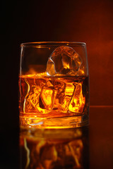 A glass of alcoholic beverage and ice on brown background