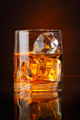 A glass of alcoholic beverage and ice on brown background