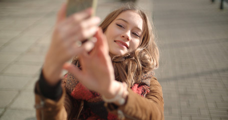 Young woman taking selfie with mobile phone in sunny city street.