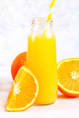 Bottles with fresh orange, apple, tomato juice and colored tubules on a gray concrete table.