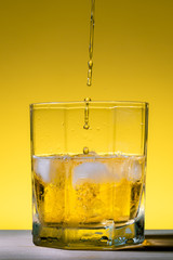 Whiskey being served in a glass with ice on a yellow background