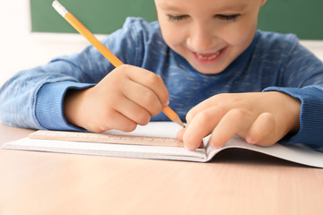 Cute little boy doing homework in classroom, closeup