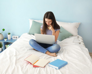 Cute teenager girl using laptop while doing homework in bedroom