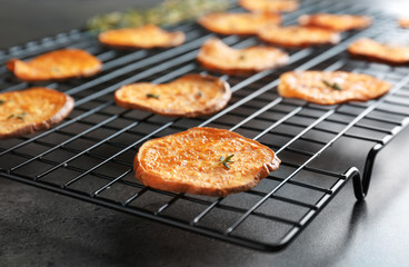Cooling rack with tasty sweet potato chips on table, closeup