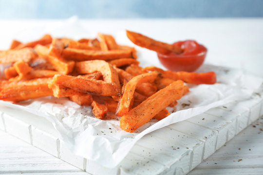 White board with tasty sweet potato fries on wooden table, closeup