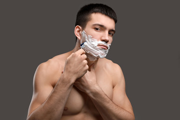 Handsome young man shaving against grey background